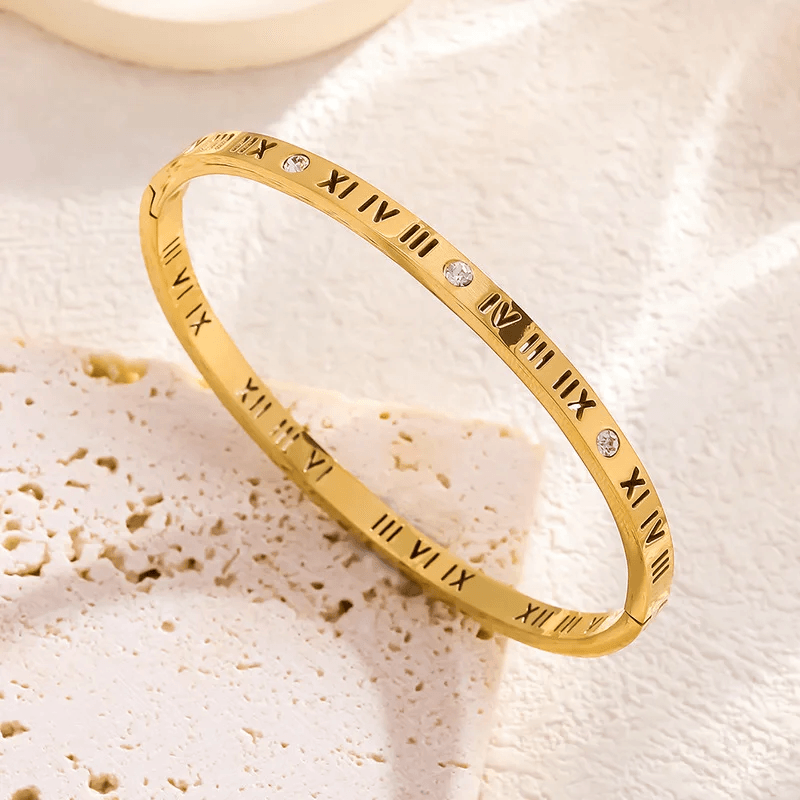 Gold bracelet with Roman numeral design on a textured beige surface