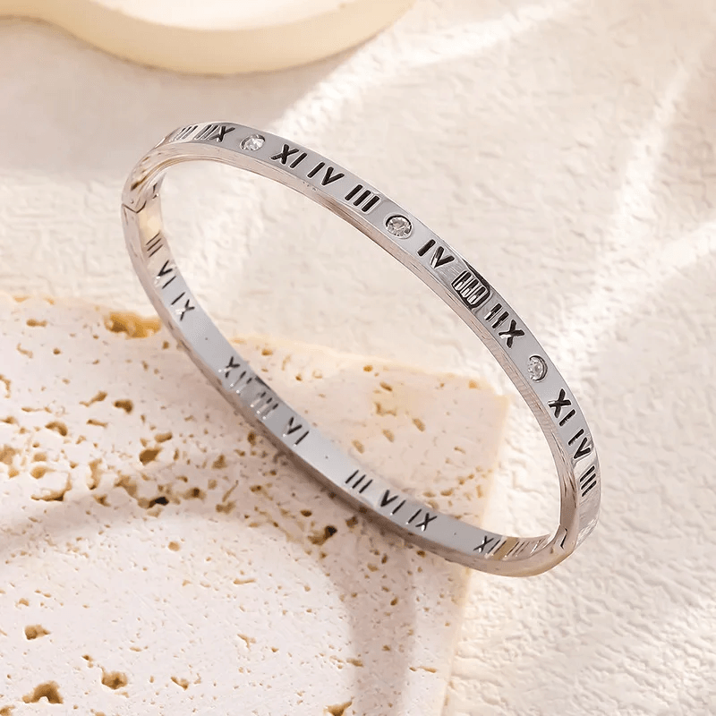 Silver bracelet with Roman numeral engraving on a textured beige surface