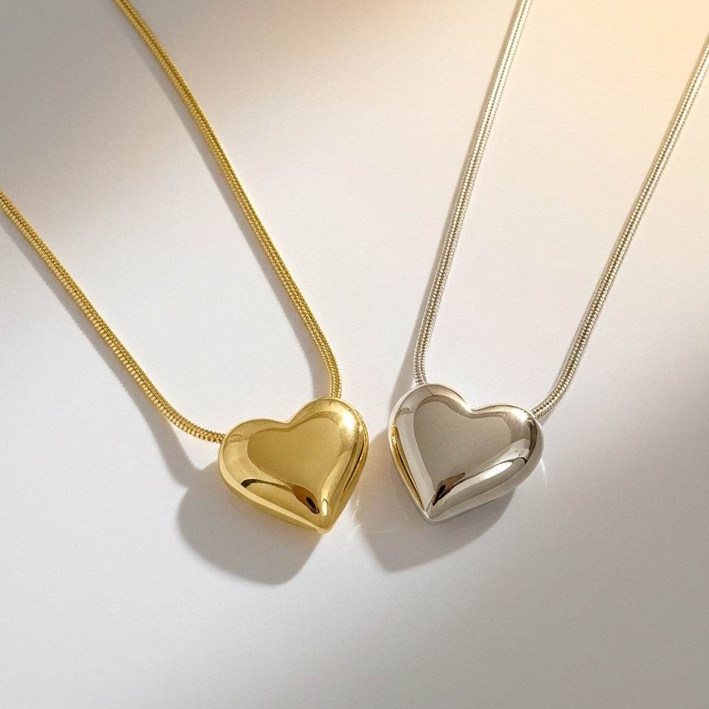 Two heart-shaped pendants, one gold and one silver, on light backgrounds.