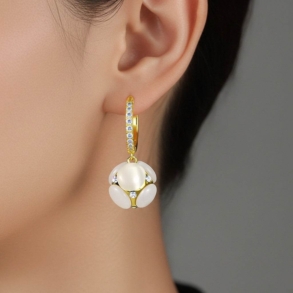 Gold earring with a white gemstone worn by a person against a neutral background