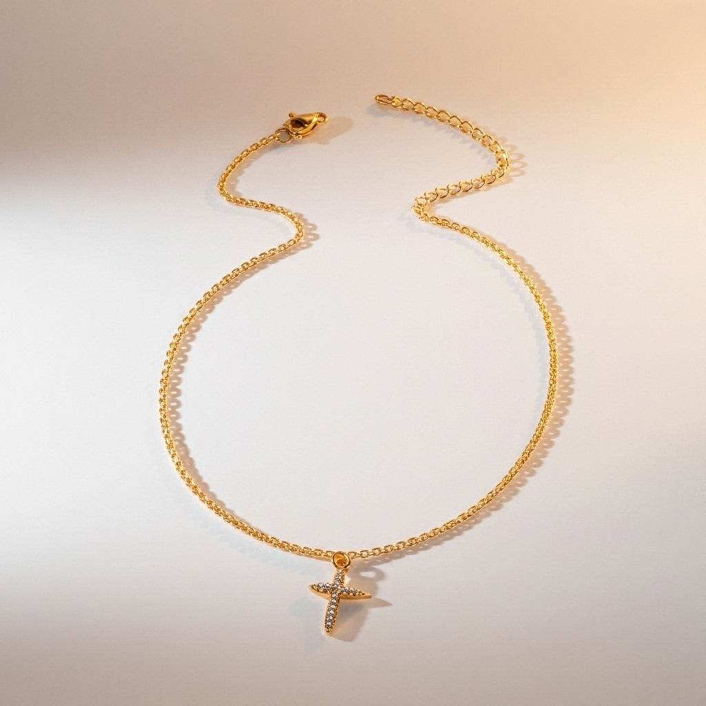 Gold anklet with a cross pendant on a light background