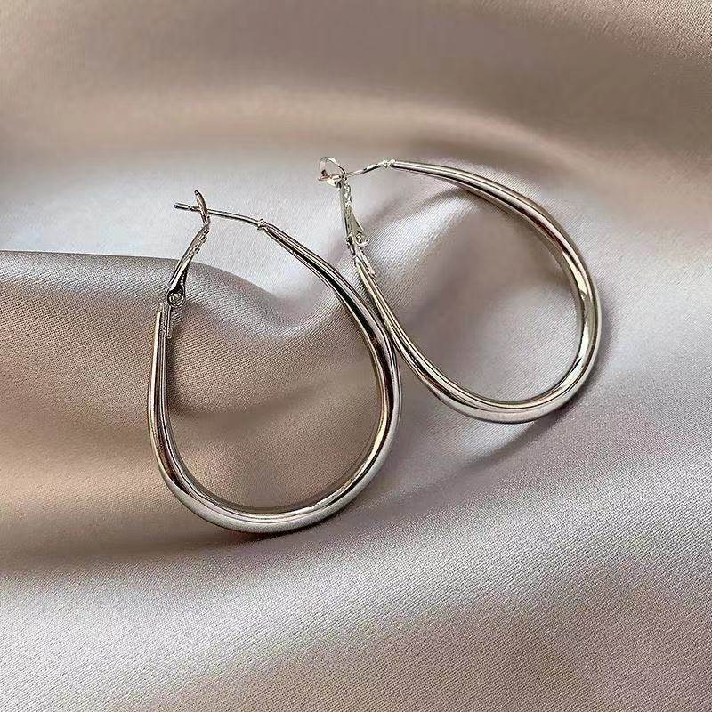 Silver hoop earrings on a beige satin surface