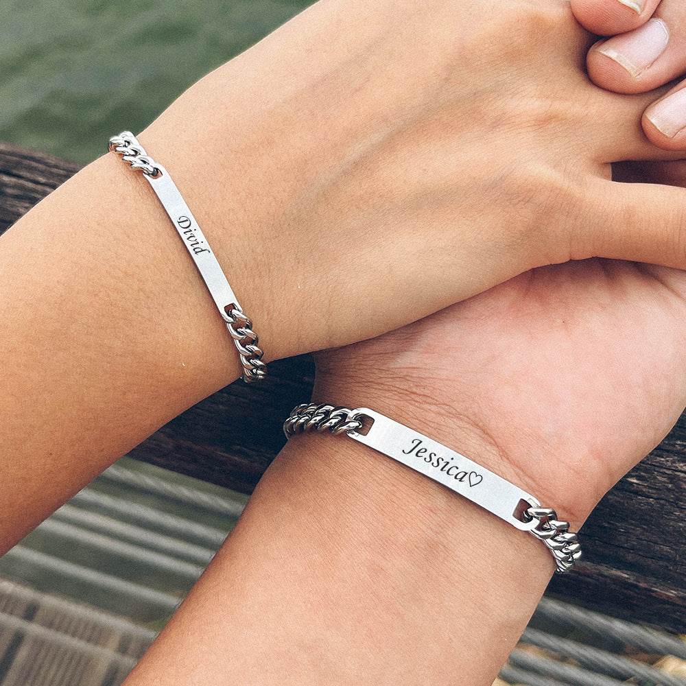 Two silver bracelets with engraved names on a person's wrist against a blurred natural background.