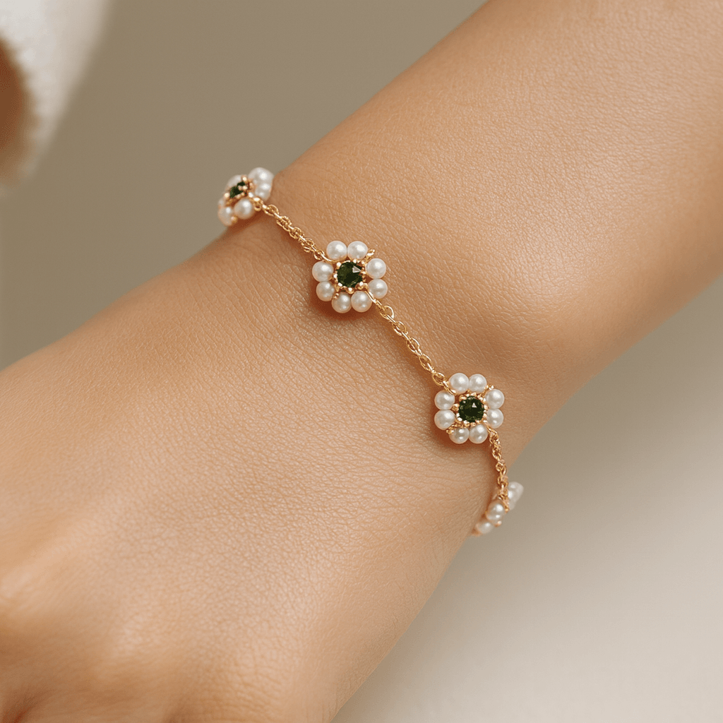 Gold bracelet with floral designs and green stones on a wrist against a neutral background